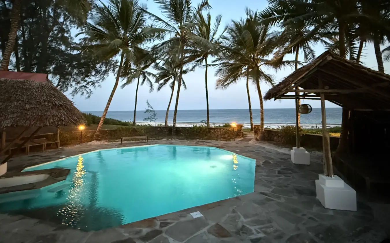 Illuminated beachfront pool with thatched structures at dusk overlooking ocean, Enkare Bofa, Kilifi, Kenya