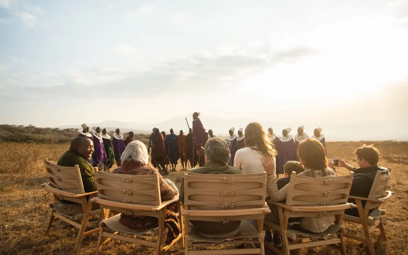 Guests seated in chairs watching Maasai warriors perform in savanna landscape, Entamanu Private, Ngorongoro Crater, Tanzania