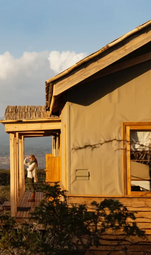 Luxury lodge with guest on wooden deck overlooking acacia trees and valley, Entamanu Private, Ngorongoro Crater, Tanzania