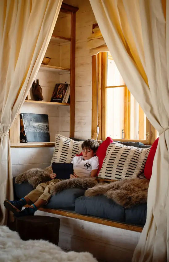 Child reading on cushioned window seat with savanna view, Entamanu Private, Ngorongoro Crater, Tanzania