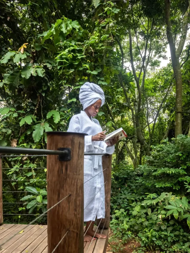 Guest reading on wooden deck overlooking forest canopy, Entebbe Forest Lodge, Entebbe and Kampala, Uganda