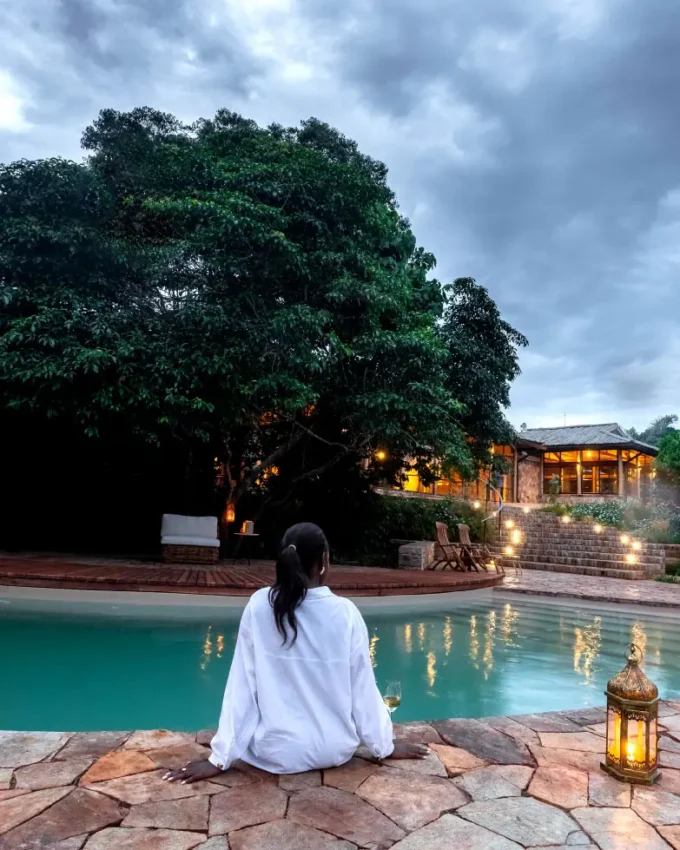 Woman sitting by illuminated pool at dusk with lodge, Entebbe and Kampala, Uganda