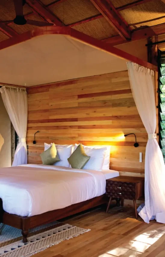 Wooden canopy bed with white linens in forest lodge bedroom, Entebbe Forest Lodge, Entebbe and Kampala, Uganda
