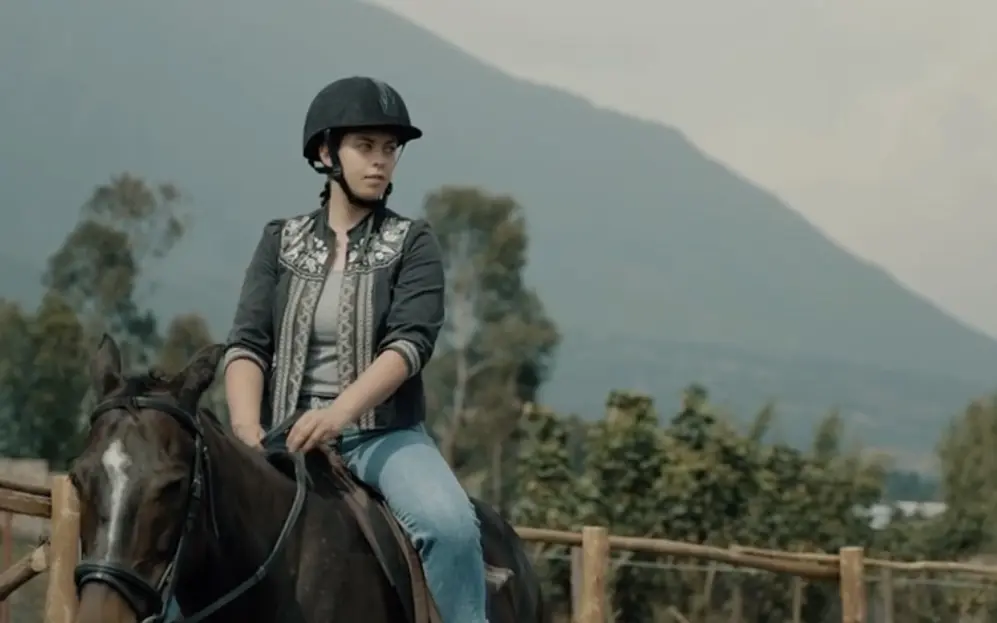 Woman riding horse on rural farm with mountain backdrop, Farmhouse Rwanda, Volcanoes National Park, Rwanda