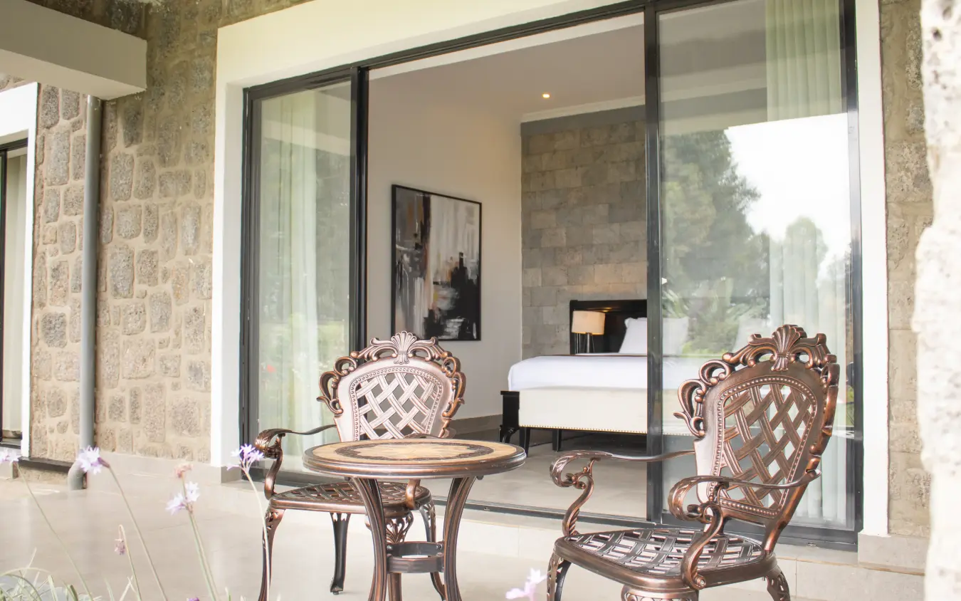 Stone patio with ornate furniture overlooking bedroom interior, Farmhouse Rwanda, Volcanoes National Park, Rwanda