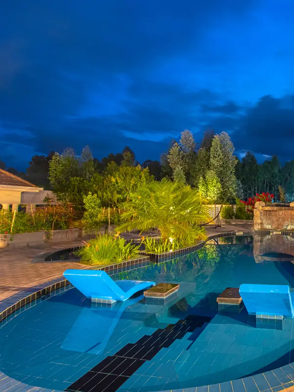 Illuminated resort pool with lounge chairs at dusk, Five Volcanoes, Volcanoes National Park, Rwanda