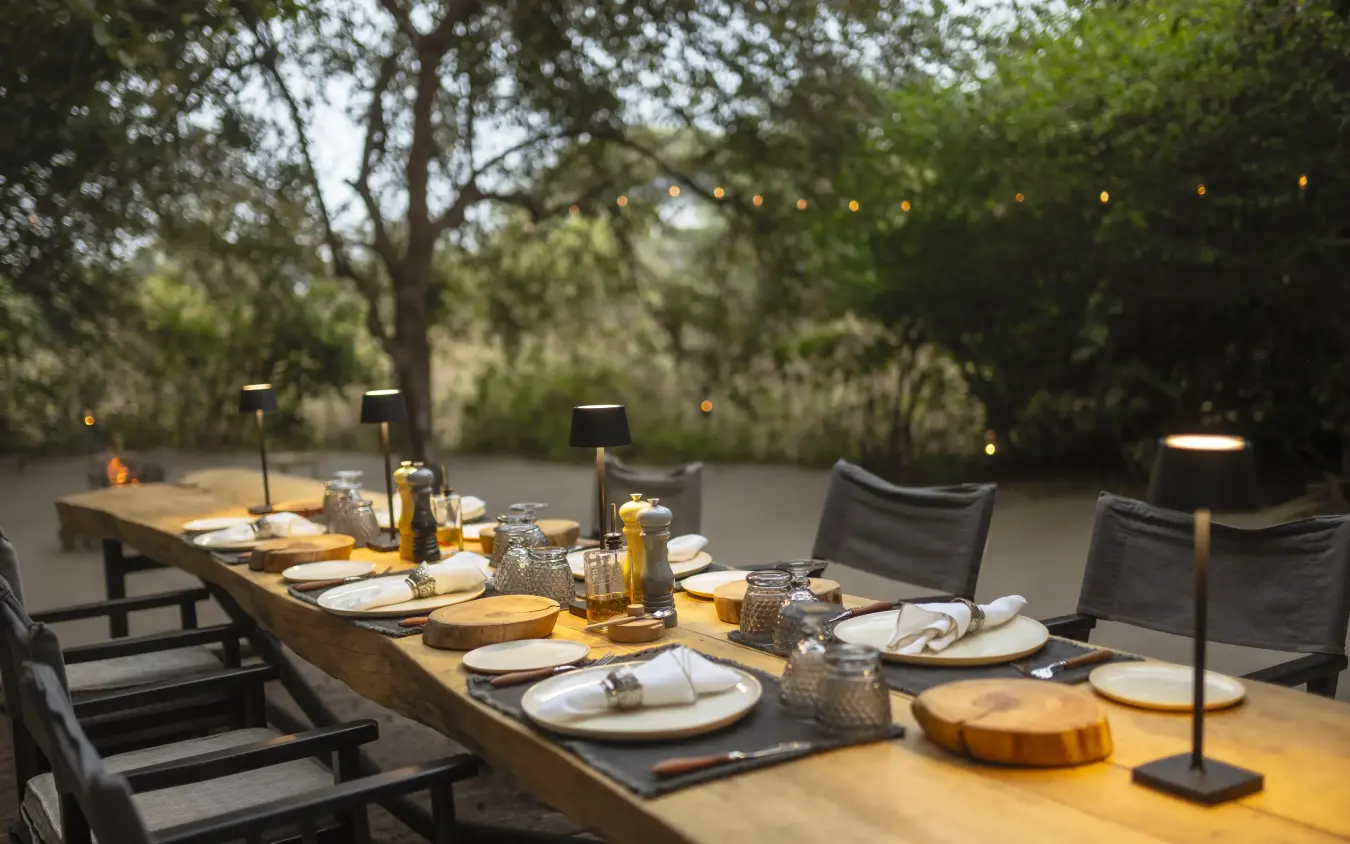 Long outdoor dining table set for evening service with forest backdrop, Forest Chem Chem, Lake Manyara, Tanzania