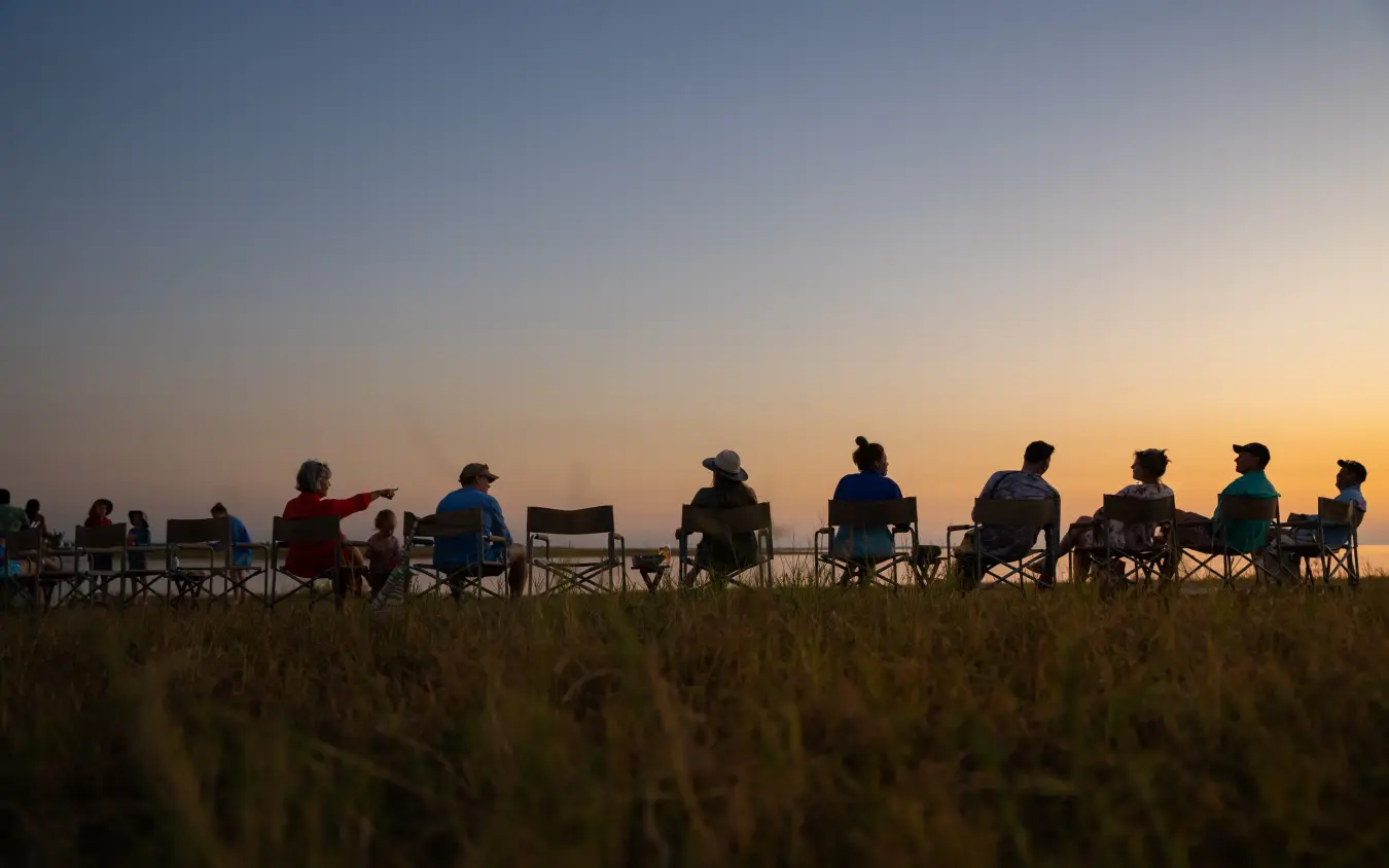 Group of guests seated in camping chairs watching sunset over grassland, Fothergill Island, Matusadona National Park, Zimbabwe