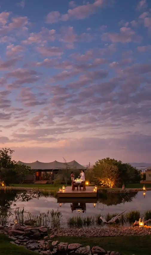 Illuminated wildlife lodge pavilions reflected in still water at dusk, Fothergill Island, Matusadona National Park, Zimbabwe