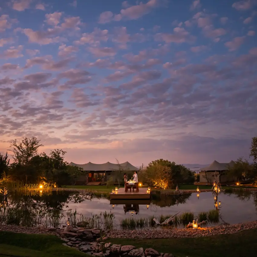 Illuminated wildlife lodge pavilions reflected in still water at dusk, Fothergill Island, Matusadona National Park, Zimbabwe