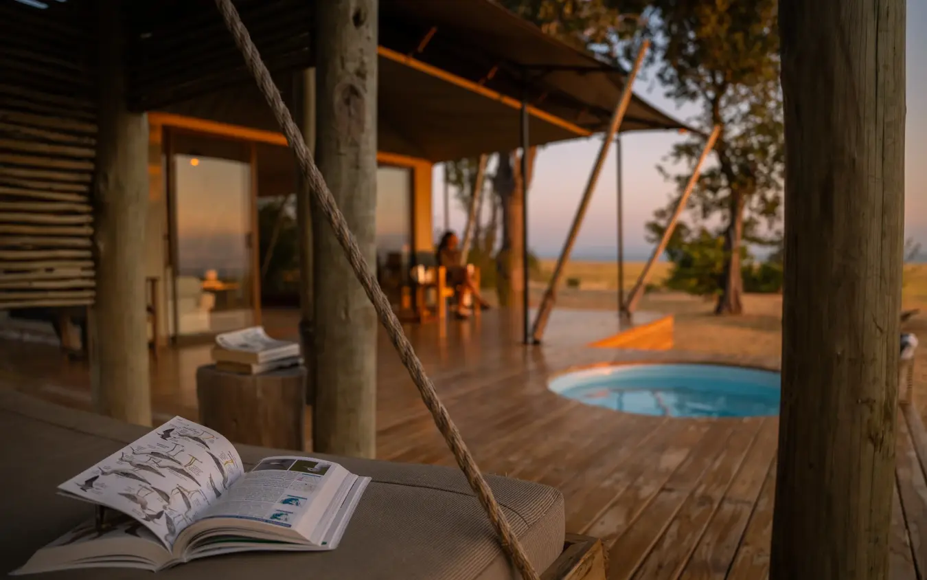 Magazine on wooden deck overlooking pool and savanna landscape at sunset, Fothergill Island, Matusadona National Park, Zimbabwe