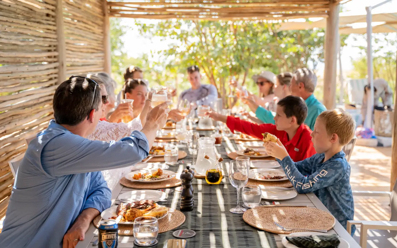 Extended family dining together under wooden pergola with garden views, Fothergill Island, Matusadona National Park, Zimbabwe