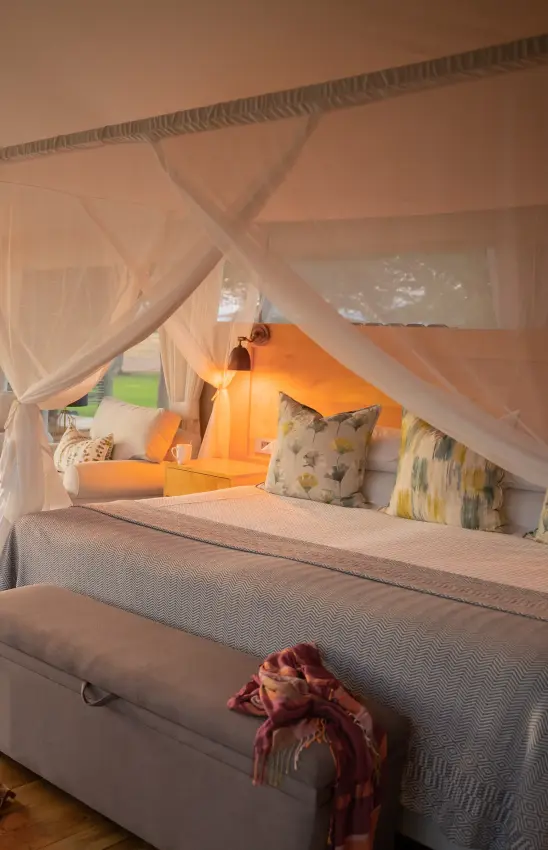 Canopy bed with sheer drapes and orange cushions in bedroom suite, Fothergill Island, Matusadona National Park, Zimbabwe