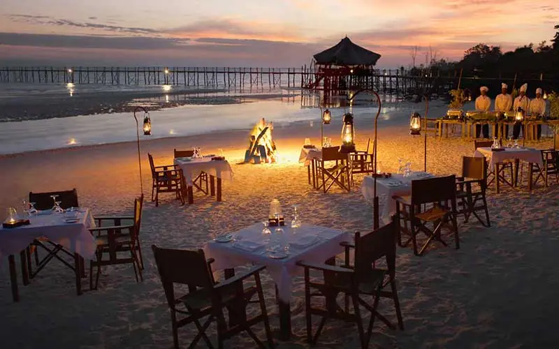 Beach dining setup at sunset with wooden chairs and tables, Fundu Lagoon, Zanzibar & Pemba, Tanzania