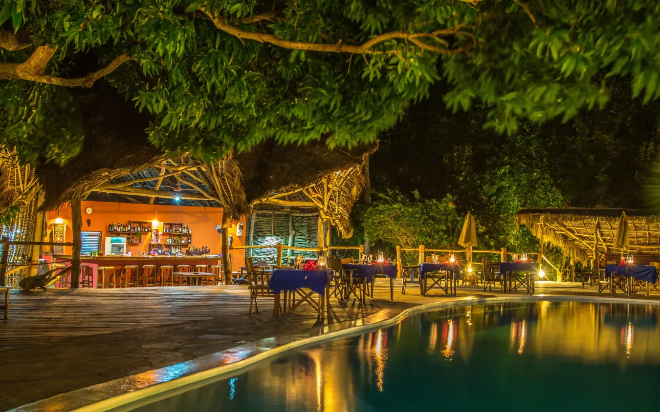 Waterfront bar and lounge area lit at night with trees, Fundu Lagoon, Zanzibar & Pemba, Tanzania
