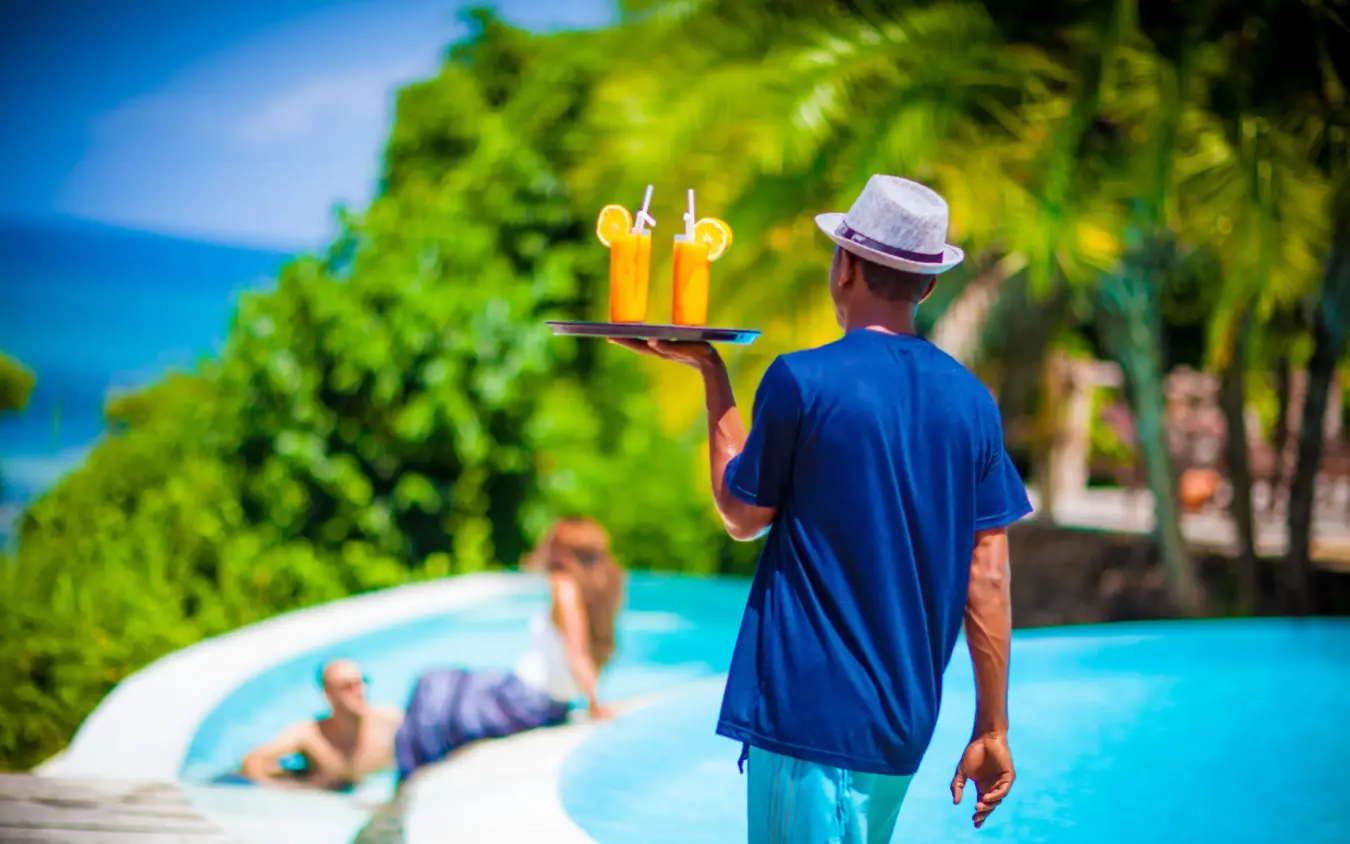 Server carrying drinks by resort pool with guests swimming, Fundu Lagoon, Zanzibar & Pemba, Tanzania