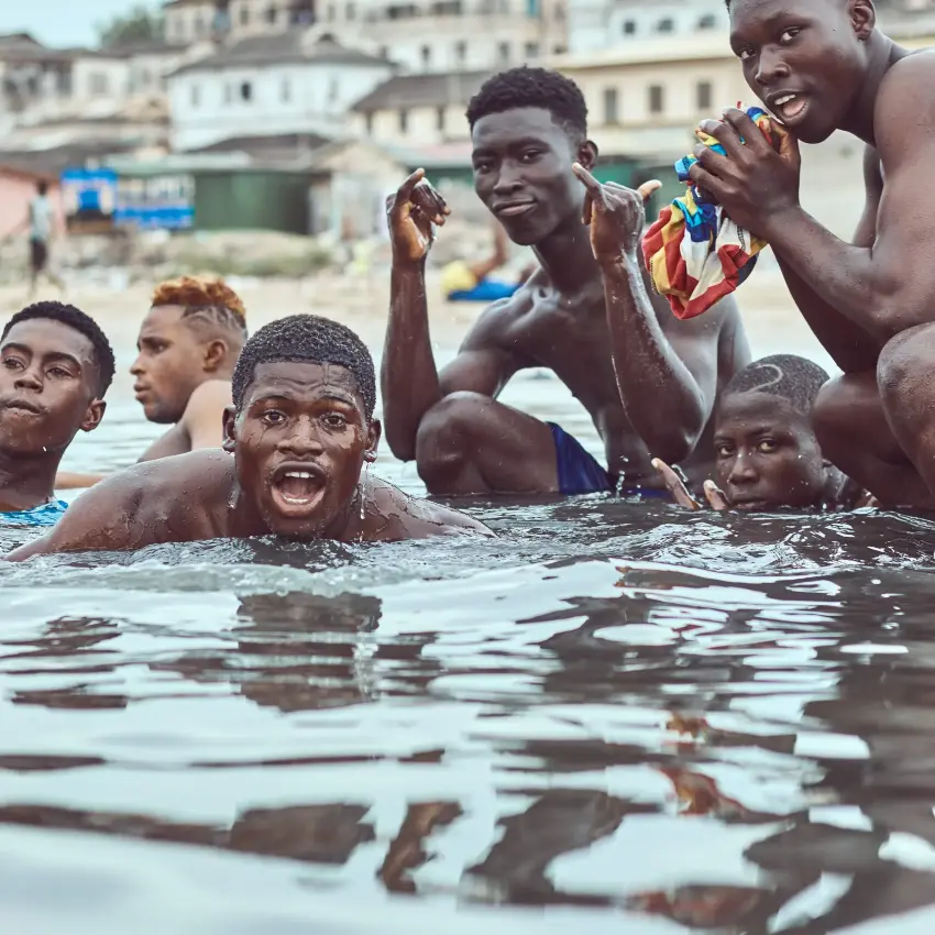 Young men swimming and laughing together on a Ghana beach shoreline