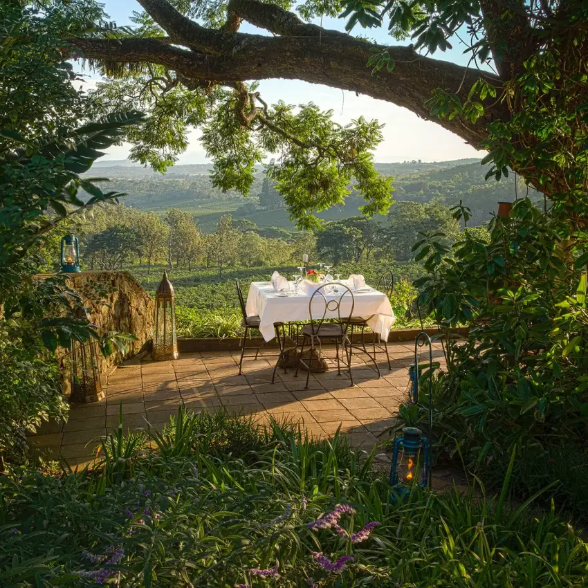 Dining table setup on wooden deck overlooking green valley, Gibb’s Farm, Ngorongoro Crater, Tanzania