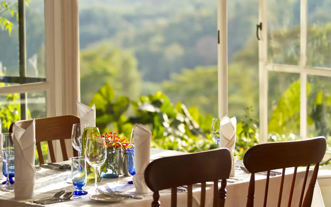 Dining room table set with mountain landscape view through windows, Gibb’s Farm, Ngorongoro Crater, Tanzania