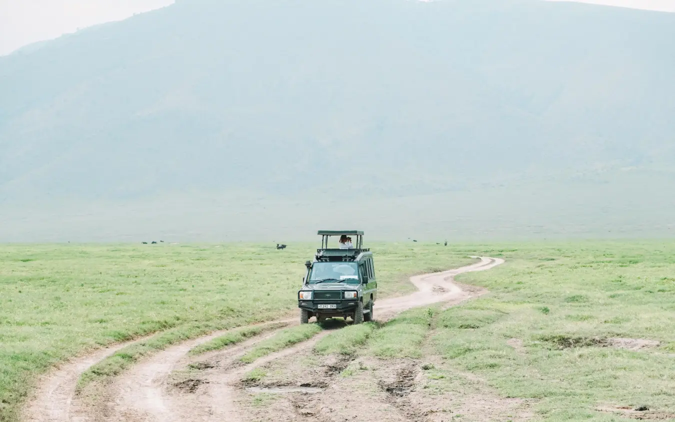 Safari vehicle driving on dirt track through grassland, Gibb’s Farm, Ngorongoro Crater, Tanzania