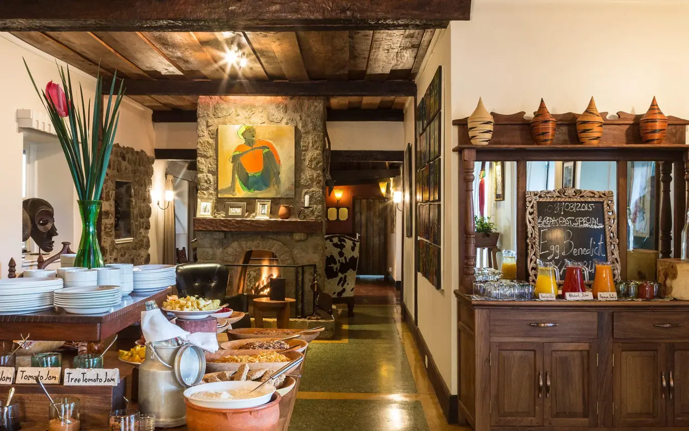 Interior lounge with fireplace, wooden furnishings, and artwork, Gibb’s Farm, Ngorongoro Crater, Tanzania