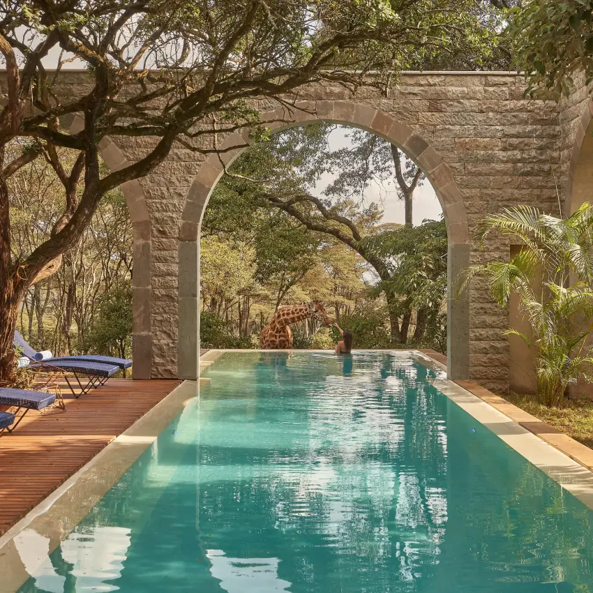 Turquoise lap pool lined with loungers beneath stone archway, Giraffe Manor, Nairobi, Kenya
