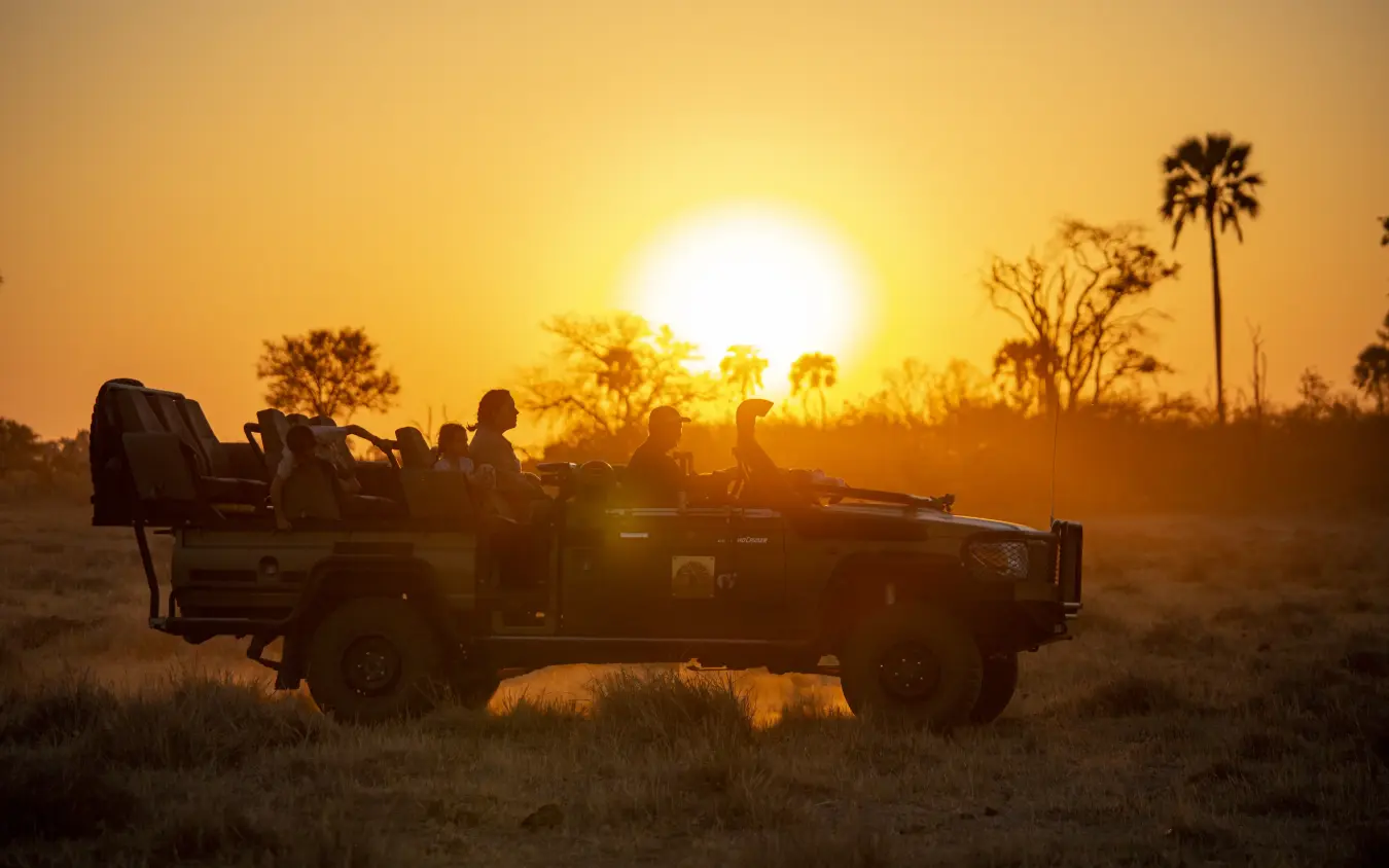 Safari vehicle with guests watching sunset over savanna, Gomoti Plains, The Okavango Delta, Botswana