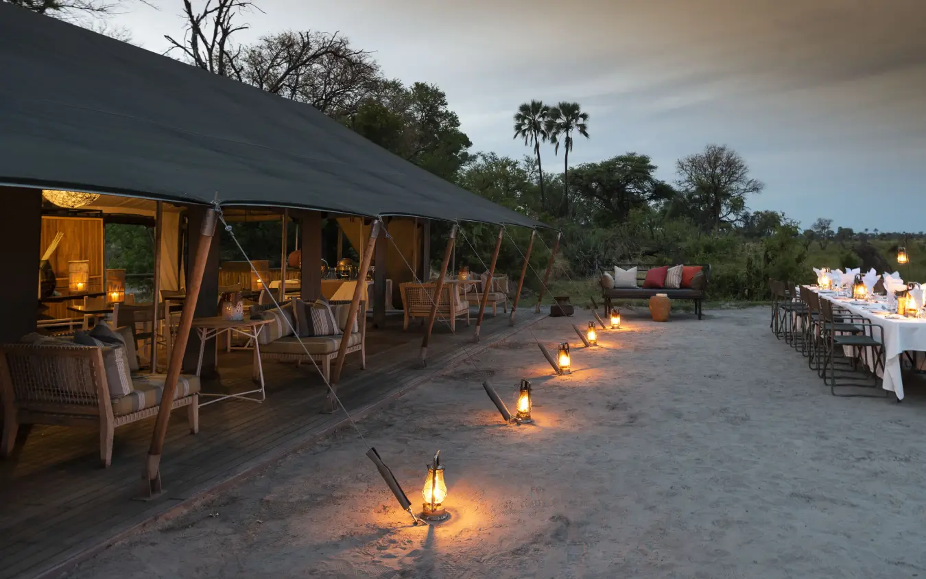 Sandy outdoor dining area with canvas tent and lanterns at dusk, Gomoti Plains, The Okavango Delta, Botswana