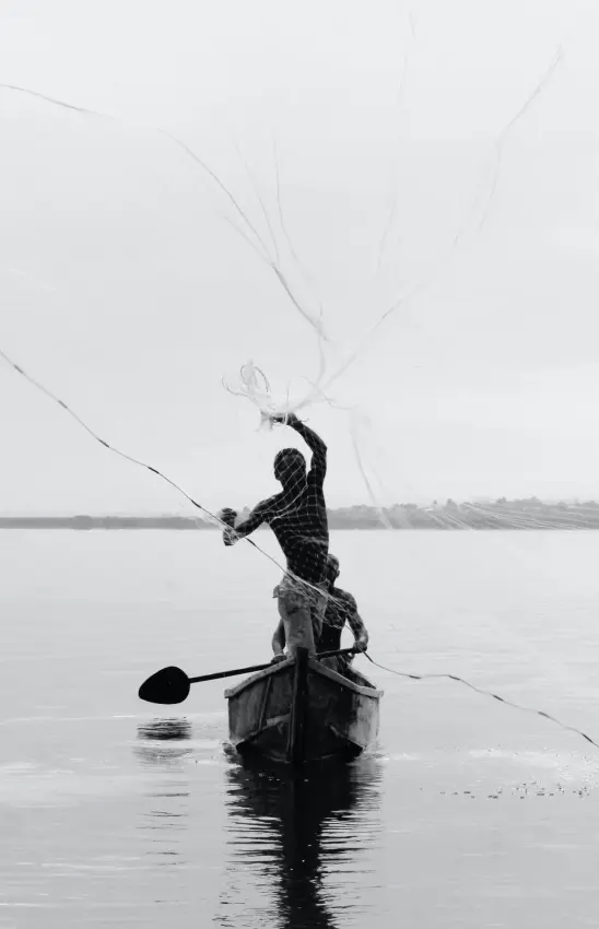 Fisherman casting net from wooden boat on calm water at dawn, Lake Kivu, Rwanda