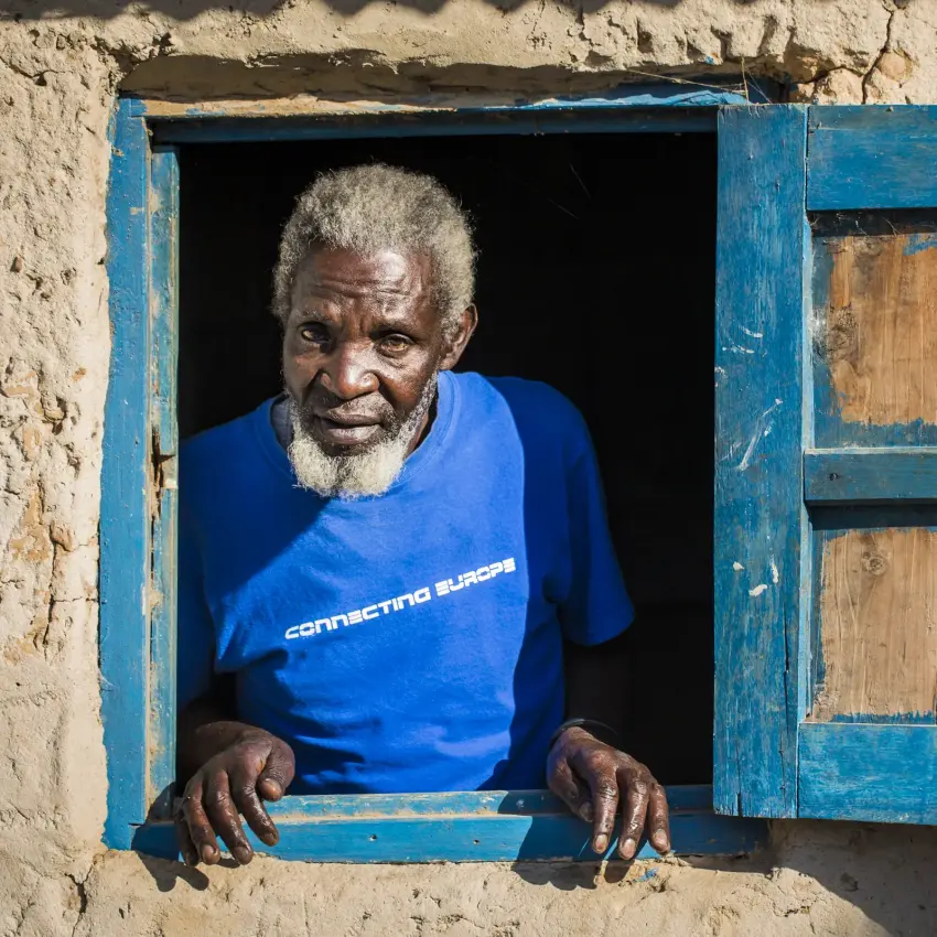 Elderly man at window of blue-painted stone building