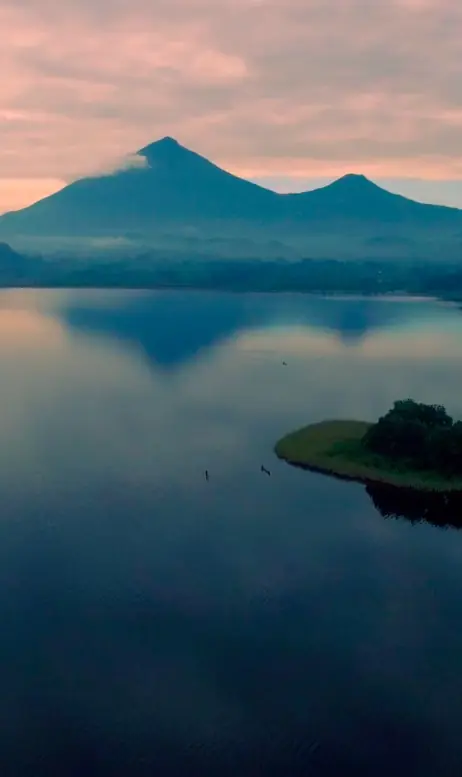 Mountain reflected in still lake at dawn with forested peninsula, Lake Kivu, Rwanda