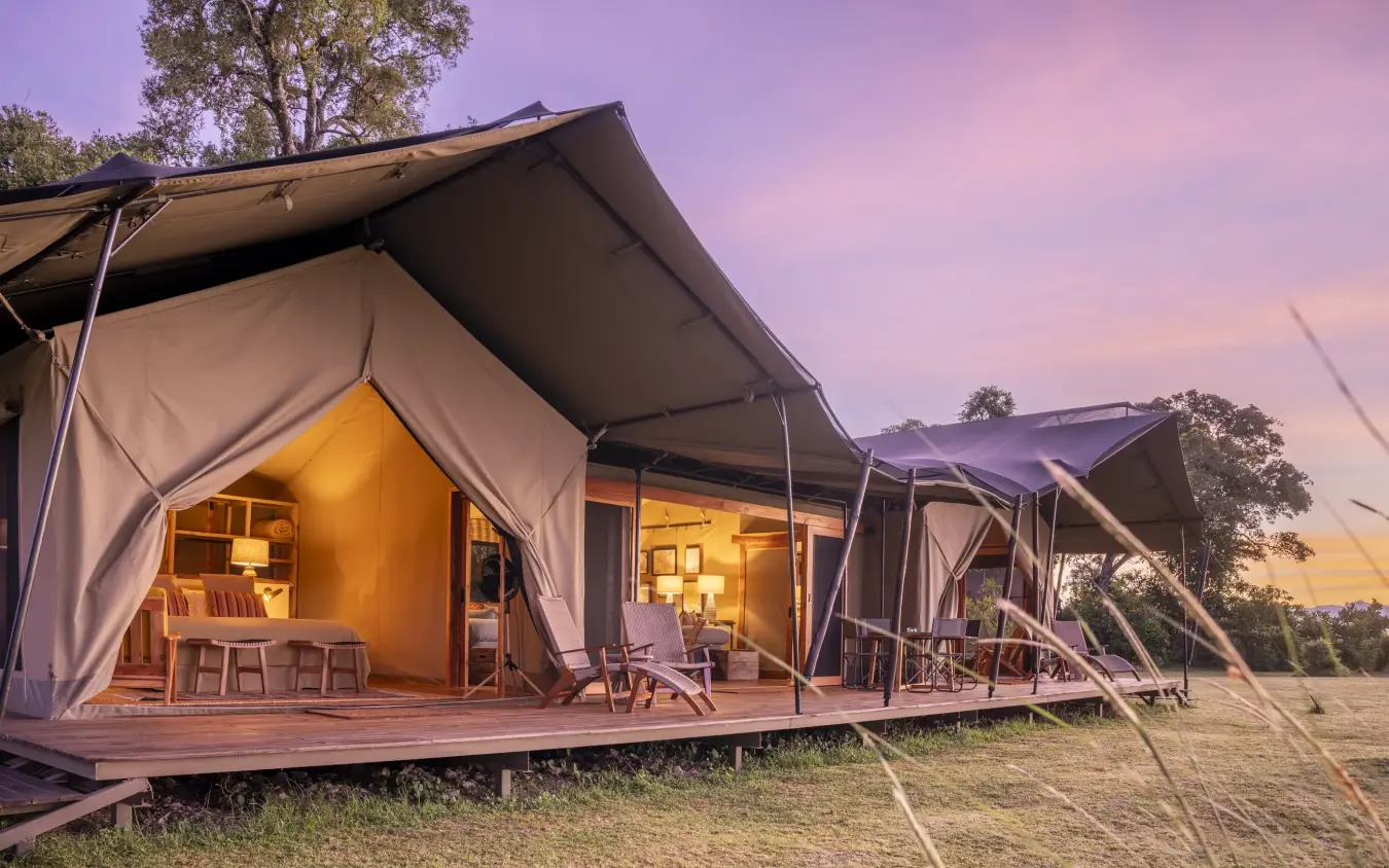Illuminated safari camp tents at dusk with wooden decking and stretched canvas, Governors’ Camp, Maasai Mara, Kenya