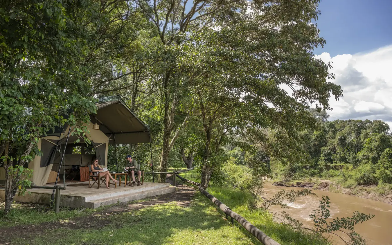 Luxury safari tent with guests on riverside deck overlooking waterhole, Governors’ Camp, Maasai Mara, Kenya