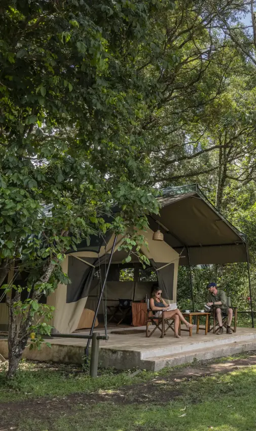 Luxury safari tent with guests on riverside deck overlooking waterhole, Governors’ Camp, Maasai Mara, Kenya