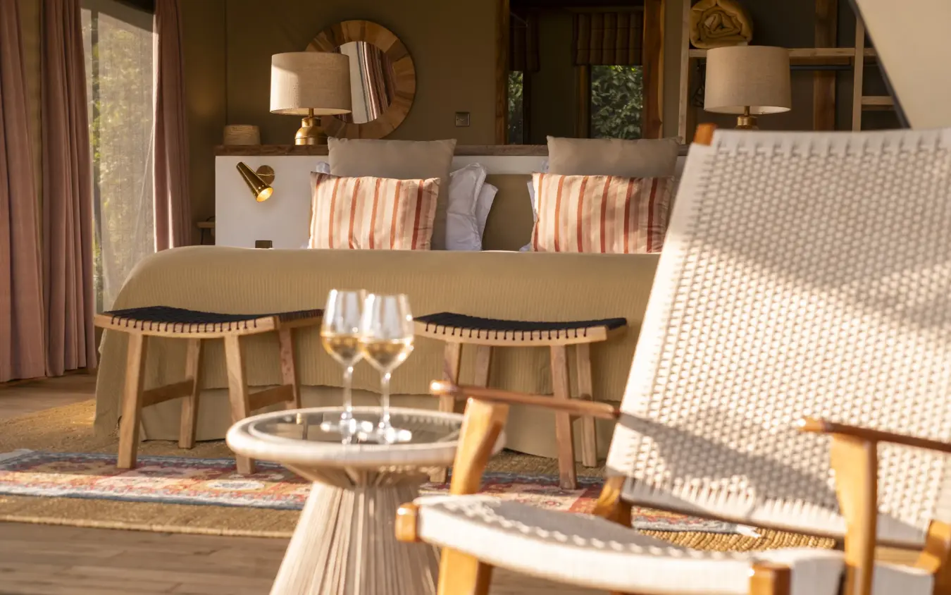 Luxury suite interior with striped pillows and wooden furniture overlooking landscape, Governors’ Camp, Maasai Mara, Kenya