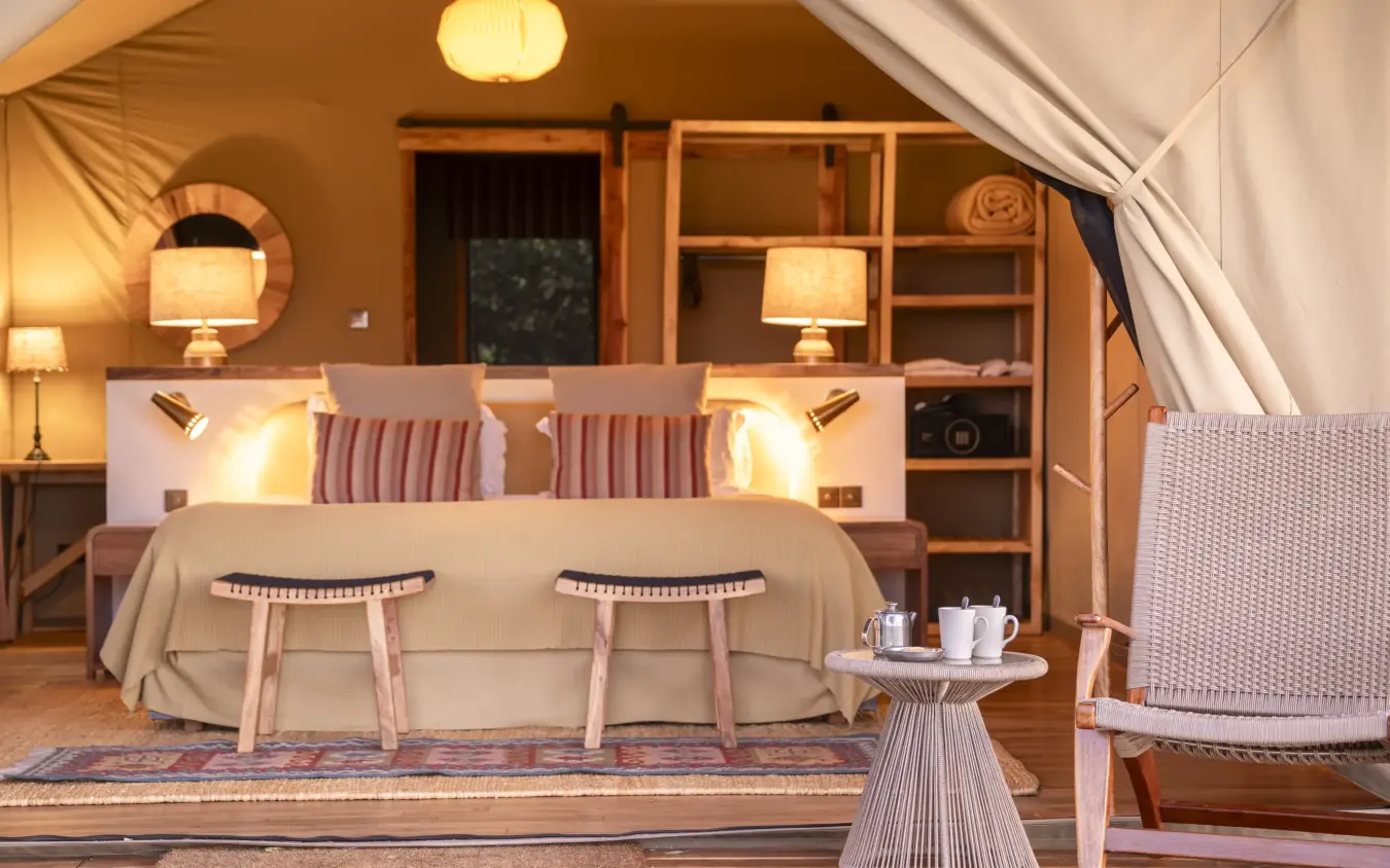 Luxury glamping tent bedroom with ambient lighting and wooden furnishings, Governors’ Camp, Maasai Mara, Kenya