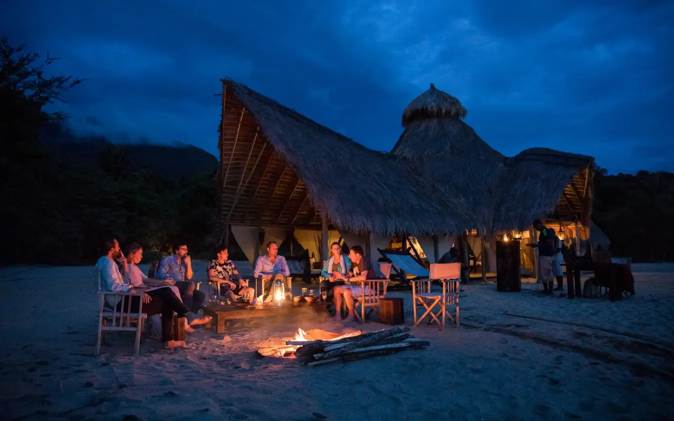 Guests gathered around campfire at beachside lodge at dusk, Greystoke Mahale, Mahale Mountains, Tanzania