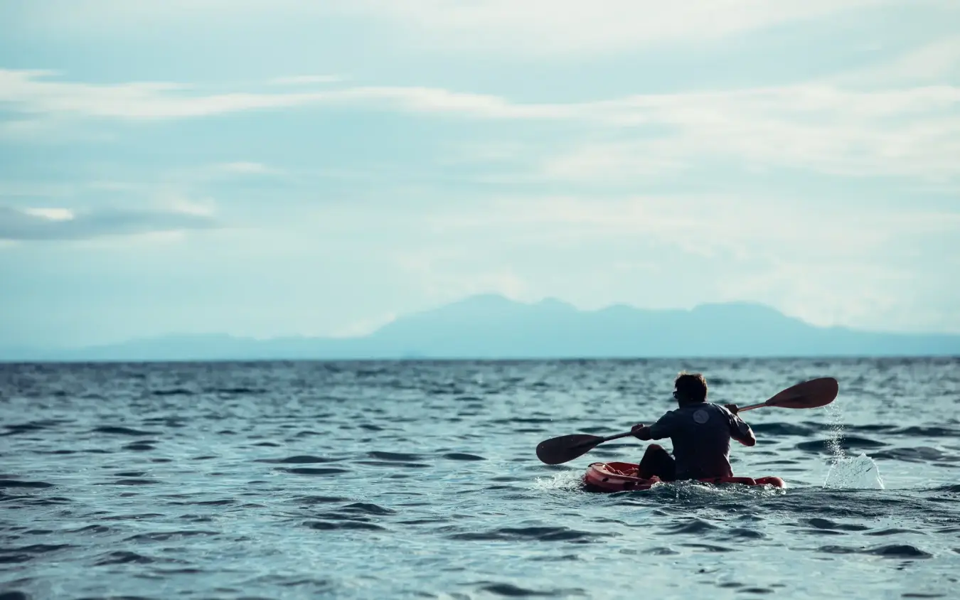 Person kayaking on open water with mountains in distance, Greystoke Mahale, Mahale Mountains, Tanzania