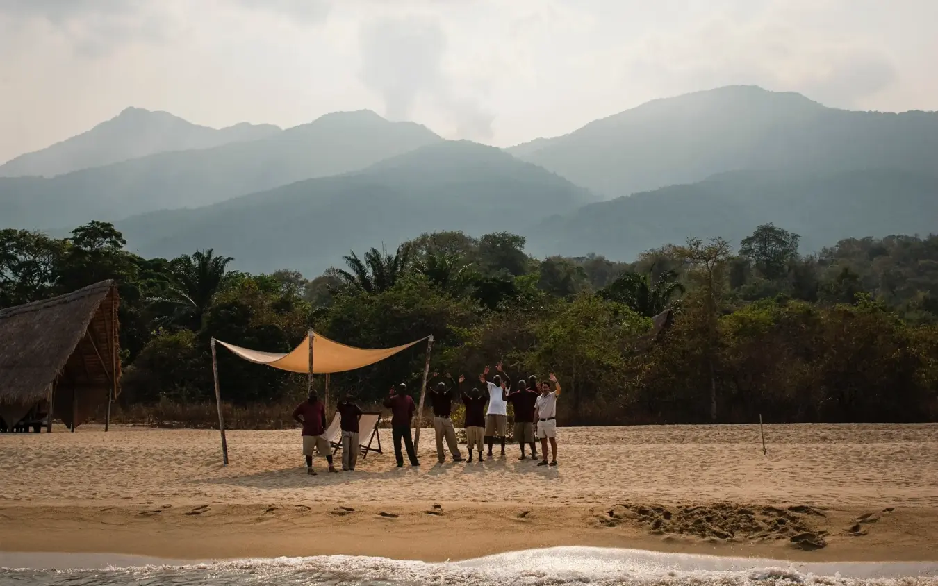 Group gathering on beach beneath mountains with orange canopy, Greystoke Mahale, Mahale Mountains, Tanzania