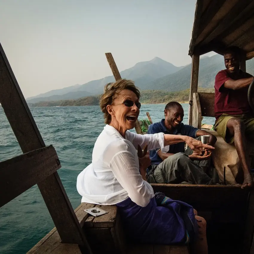 Guests in wooden boat on lake with mountain backdrop, Greystoke Mahale, Mahale Mountains, Tanzania