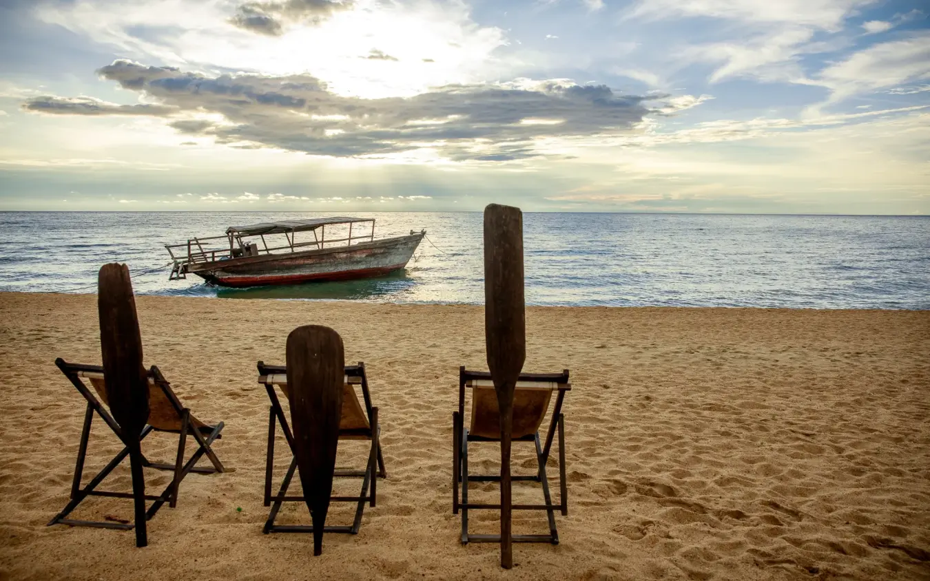 Three wooden chairs facing ocean with moored boat, Greystoke Mahale, Mahale Mountains, Tanzania
