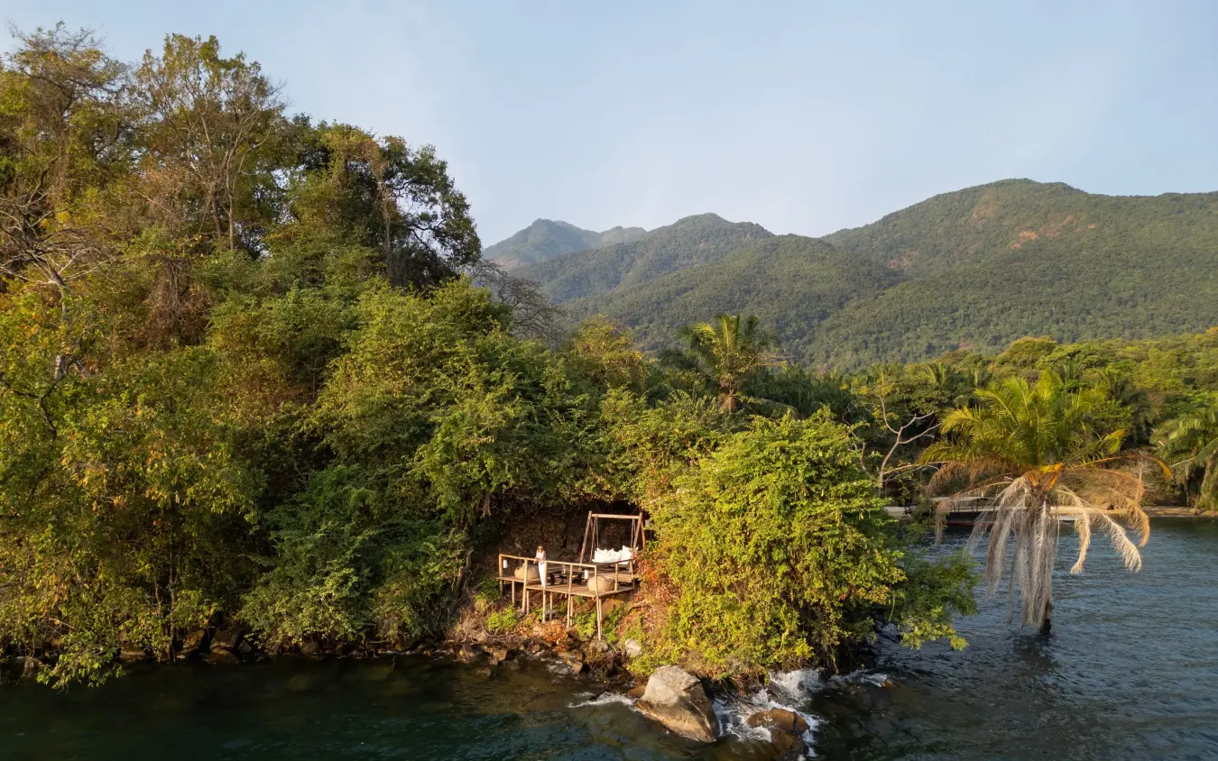Wooden deck overlooking river with forested mountains beyond, Greystoke Mahale, Mahale Mountains, Tanzania