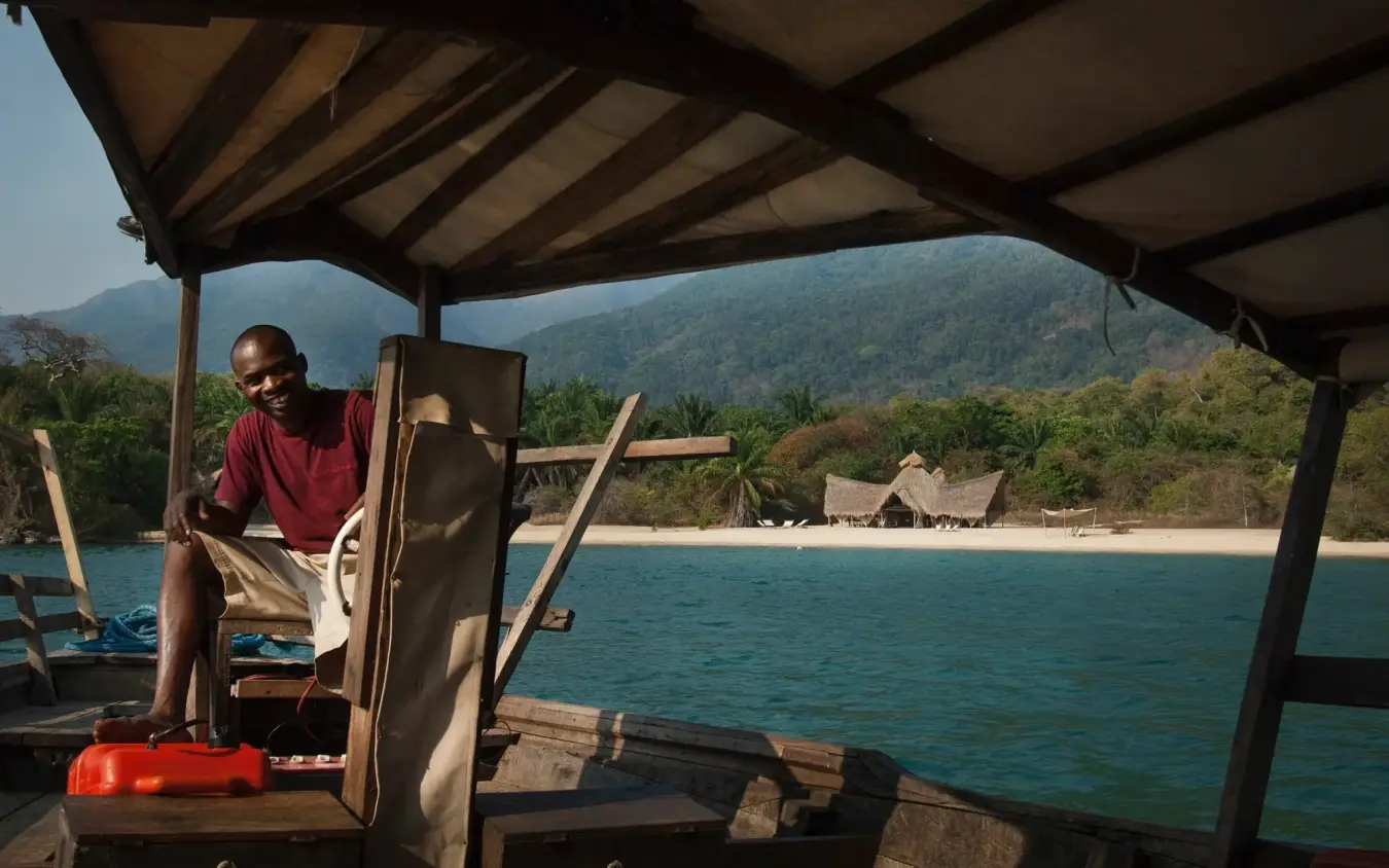 Man sitting on boat deck overlooking turquoise water and beach, Greystoke Mahale, Mahale Mountains, Tanzania