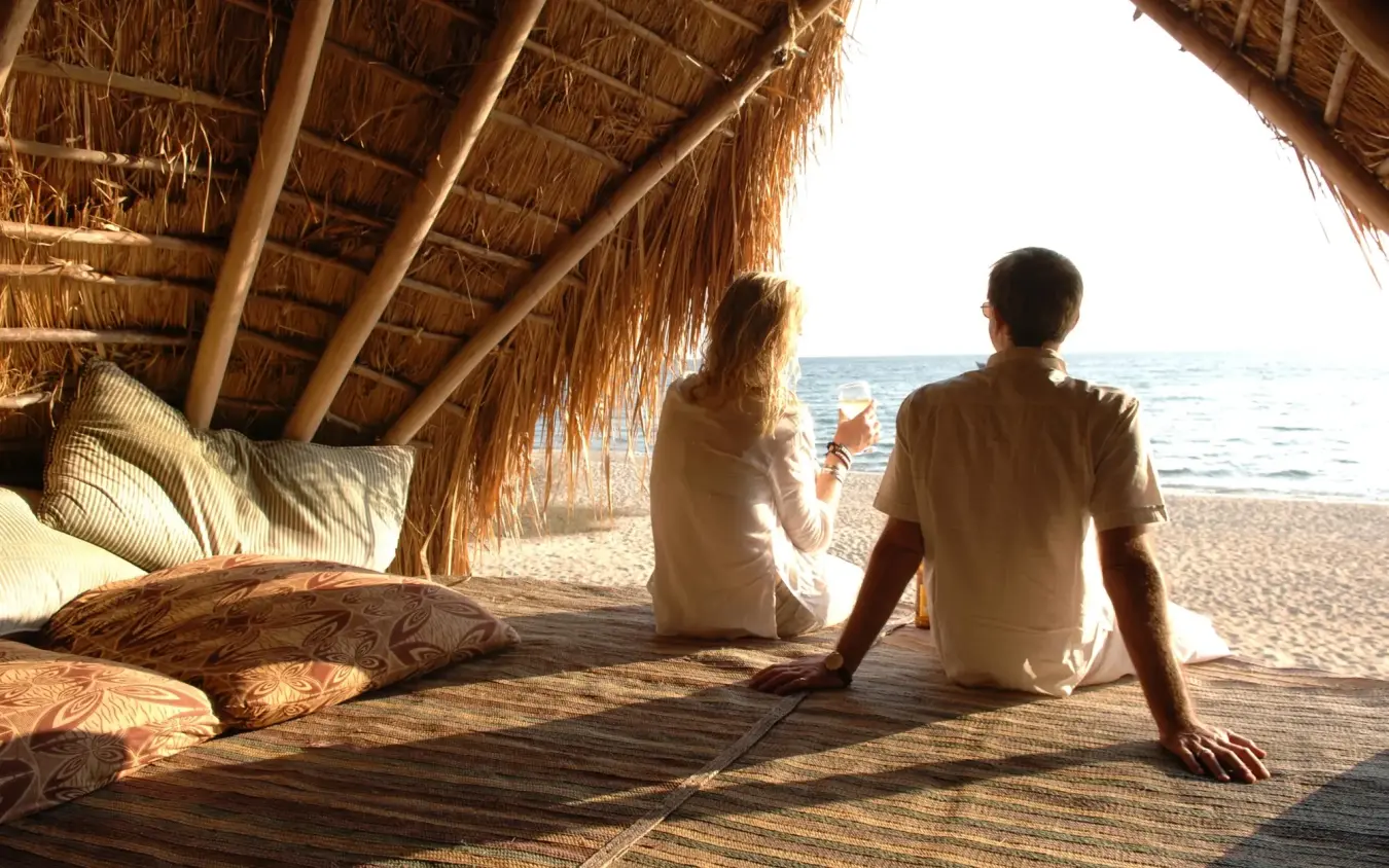 Couple relaxing in beachfront shelter overlooking ocean, Greystoke Mahale, Mahale Mountains, Tanzania