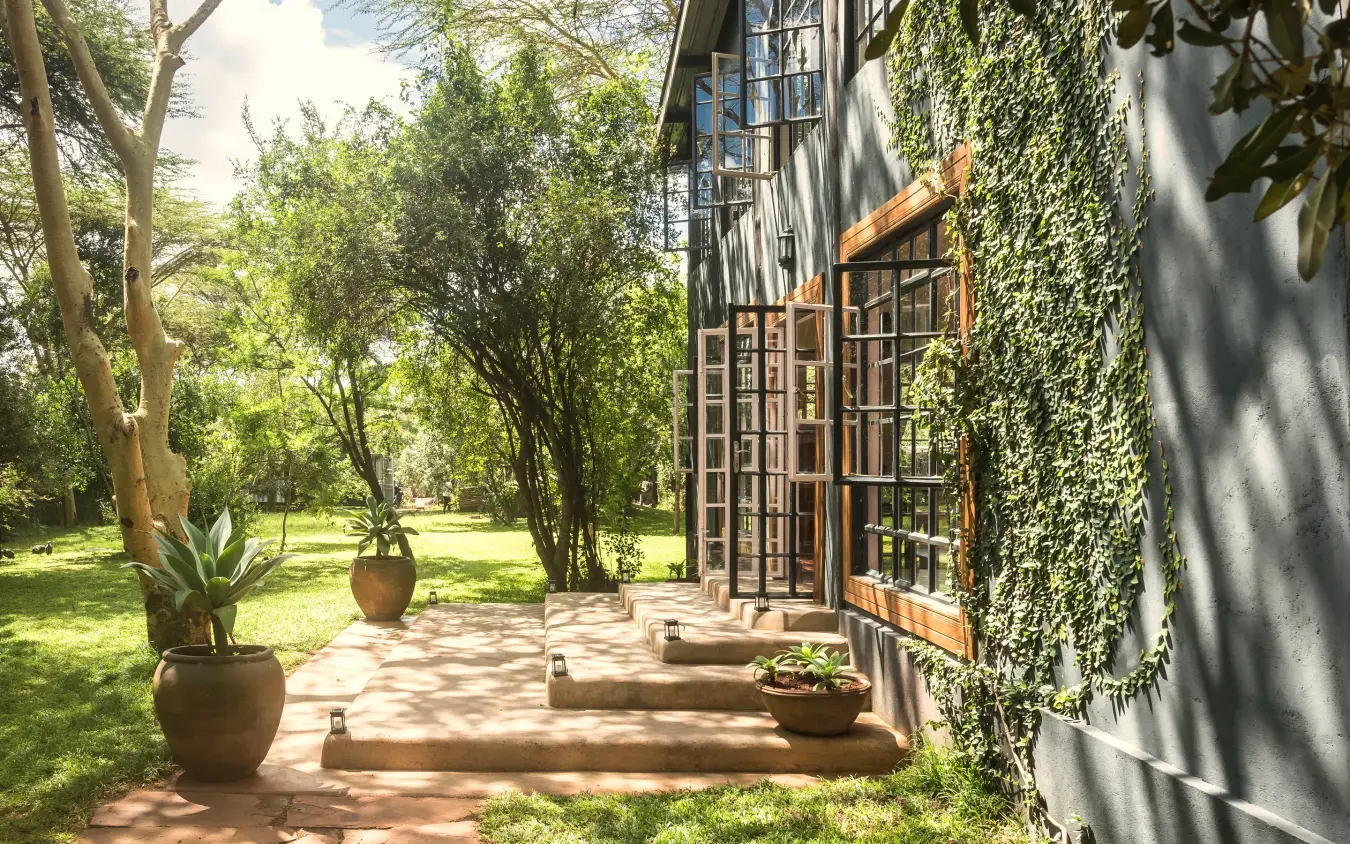 Ivy-covered building with wooden doors and shaded garden pathway, Hemingways Eden Residence, Nairobi, Kenya