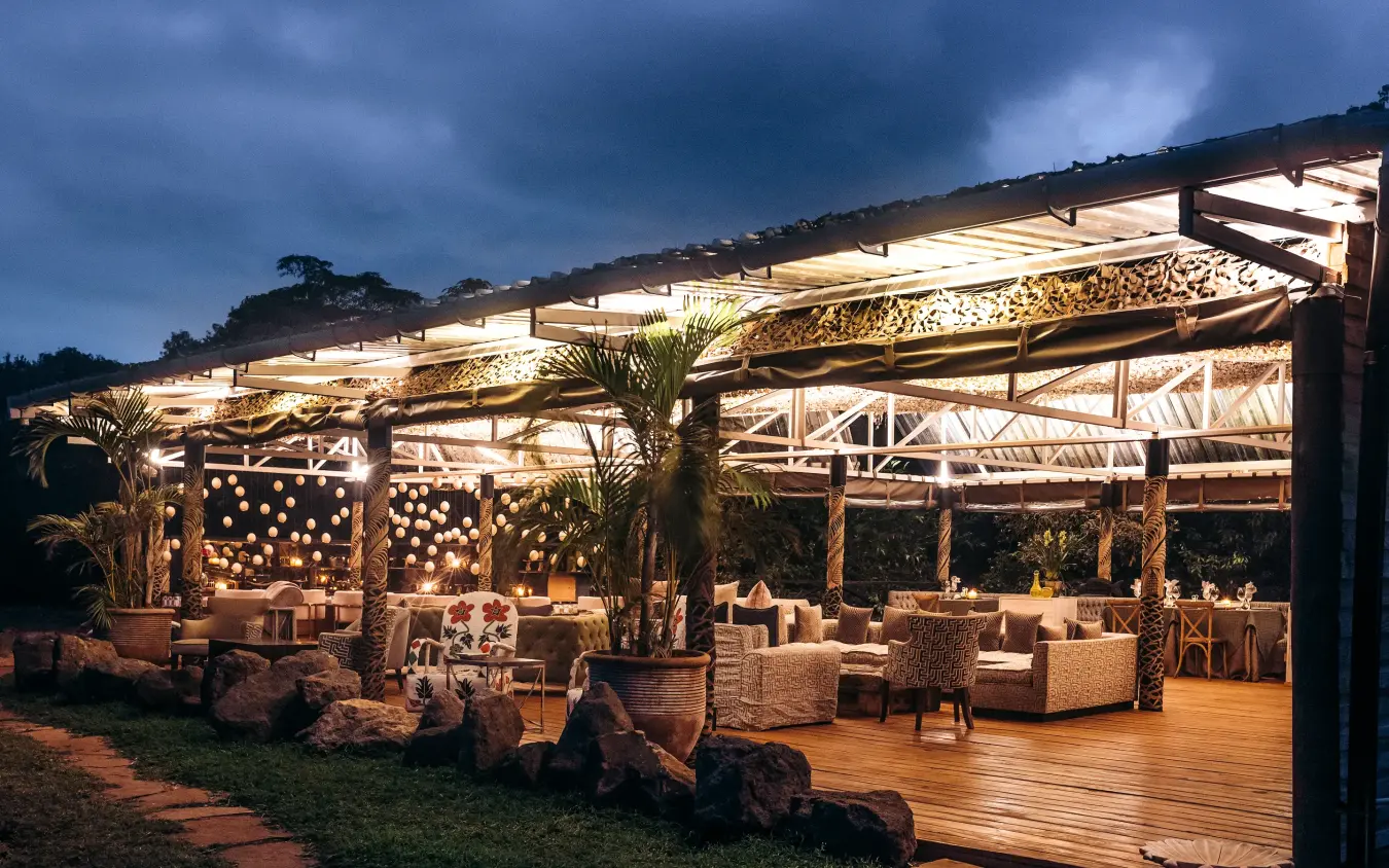 Illuminated covered terrace with seating and palm trees at dusk, Hemingways Eden Residence, Nairobi, Kenya