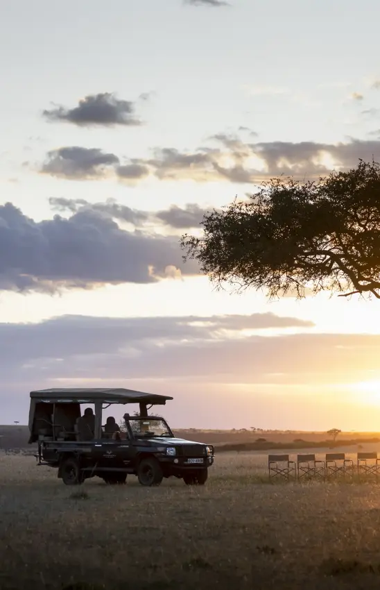 Safari vehicle with guests watching sunset over African savanna grassland, Hemingways Ol Seki Mara, Maasai Mara, Kenya