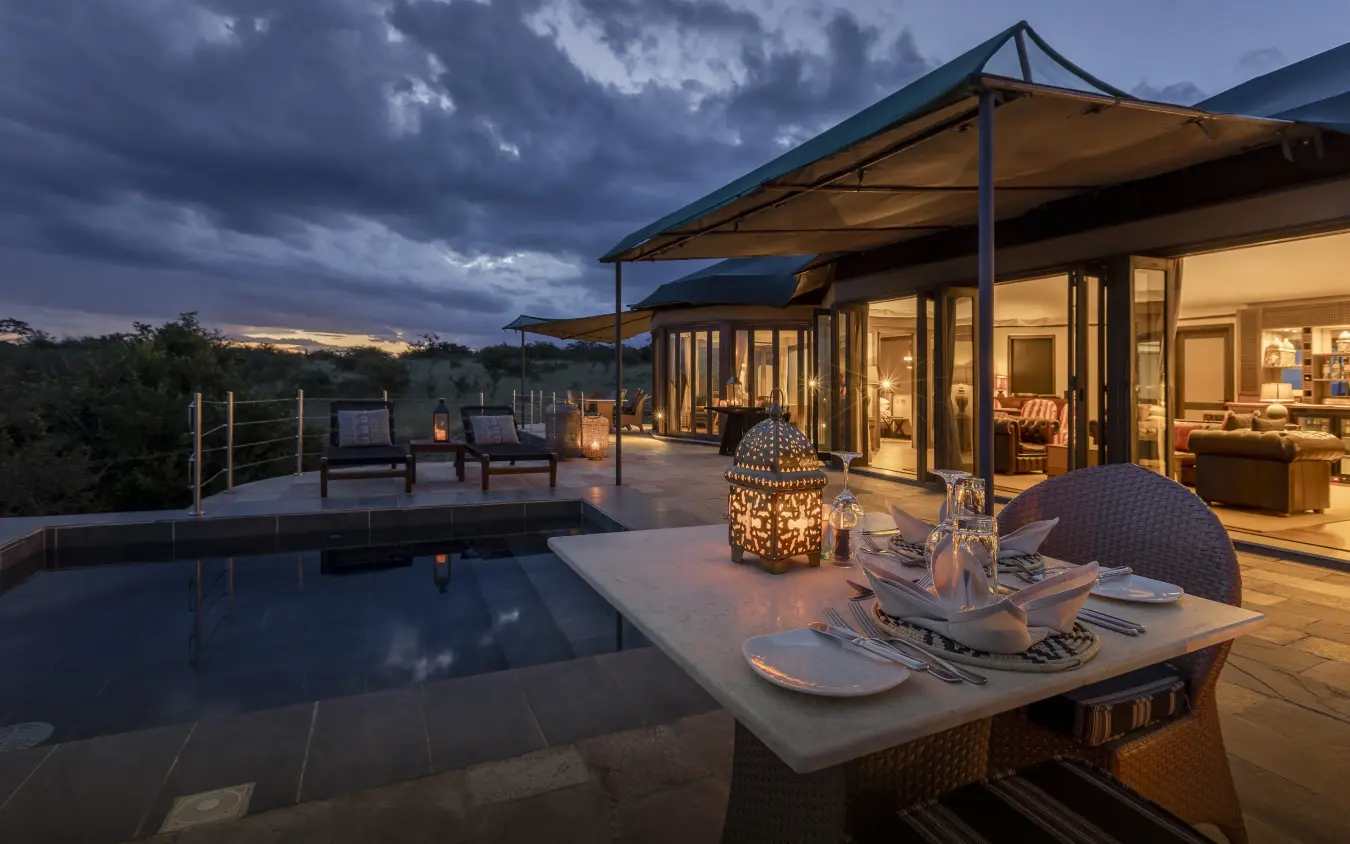 Twilight view of luxury lodge terrace with pool and dining area overlooking savanna, Hemingways Ol Seki Mara, Maasai Mara, Kenya