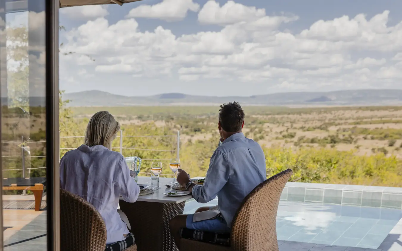 Couple dining on terrace overlooking vast savanna landscape, Hemingways Ol Seki Mara, Maasai Mara, Kenya