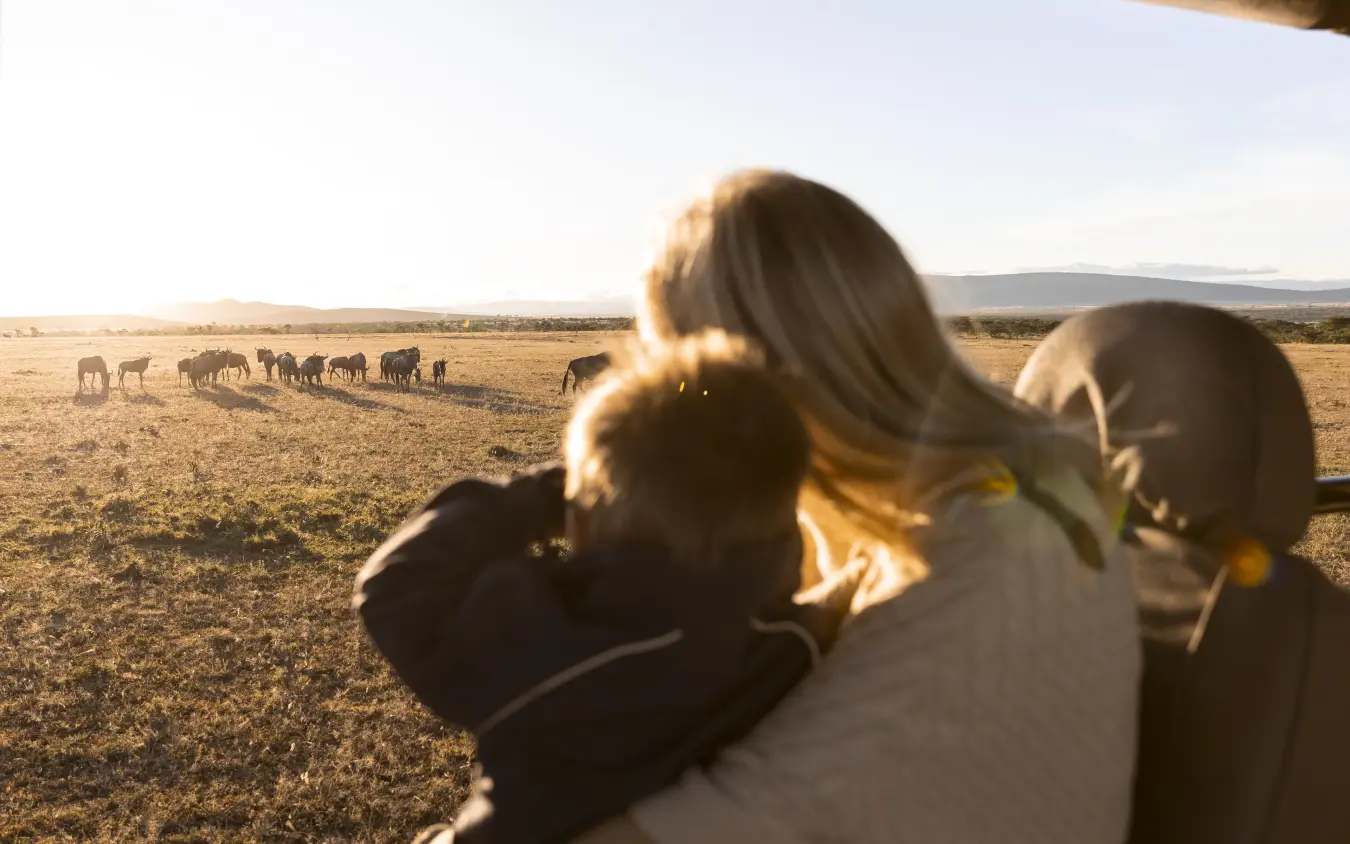 Woman with child viewing elephants grazing in distant grassland at golden hour, Hemingways Ol Seki Mara, Maasai Mara, Kenya